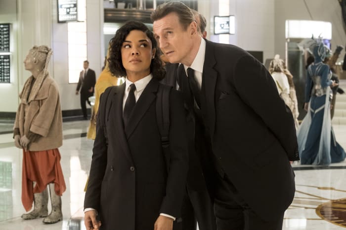 Agent M and High T (Liam Neeson), in his three-piece suit complete with a pocket square and pocketwatch chain, plus very fashion-forward aliens in the background. Photo: Giles Keyte/Sony Pictures Entertainment
