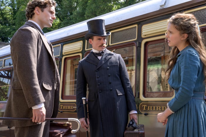 'He’s very at ease in his costume, so that gave an aura of loosening of things, as well as, the strength of the silhouette,' says Boyle, about the "fresh" new take on Sherlock, as played by Superman (Cavill, left), with a disapproving Mycroft and a hat and gloveless Enola.