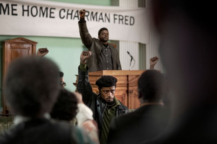 William "Bill" O'Neal (Lakeith Stanfield, center front) and Chairman Fred at the podium.