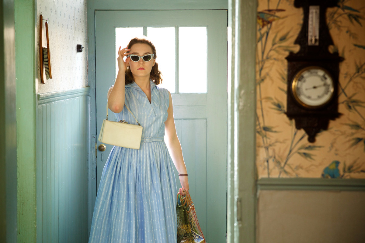 Eilis in a blue dress, statement sunglasses and a recyclable shopping bag. (That's so 2015.) Photo: Kerry Brown/Twentieth Century Fox Film Corporation