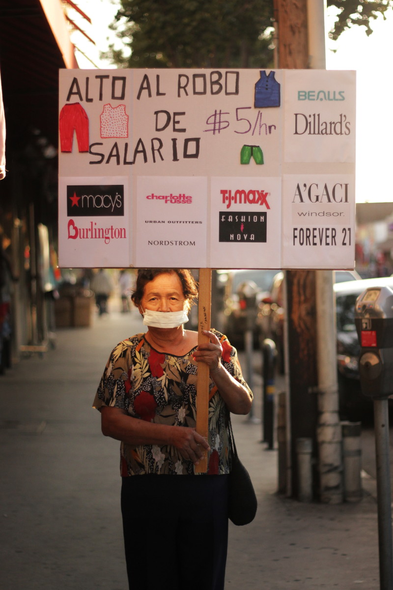 Juliana Bautista poses in November 2017 with a protest sign targeting brands and retailers that were found to have flagrant labor violations in L.A.
