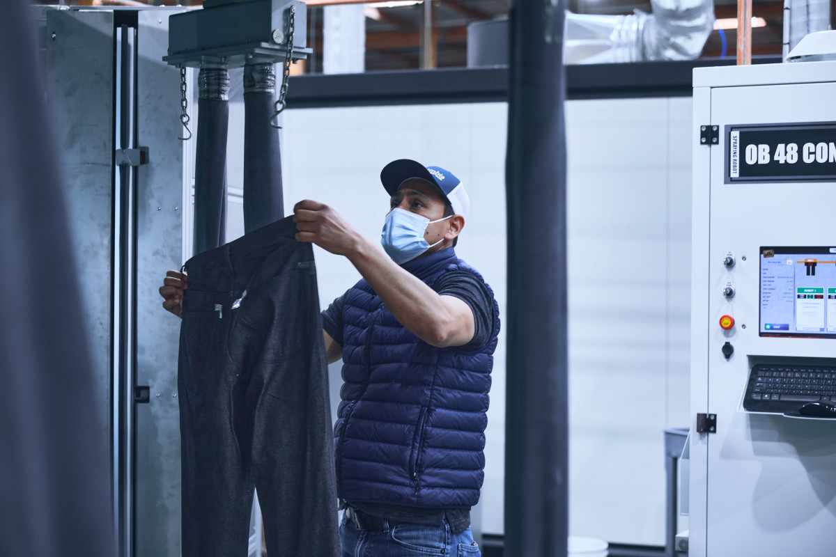 An employee places raw jeans on an automated machine.
